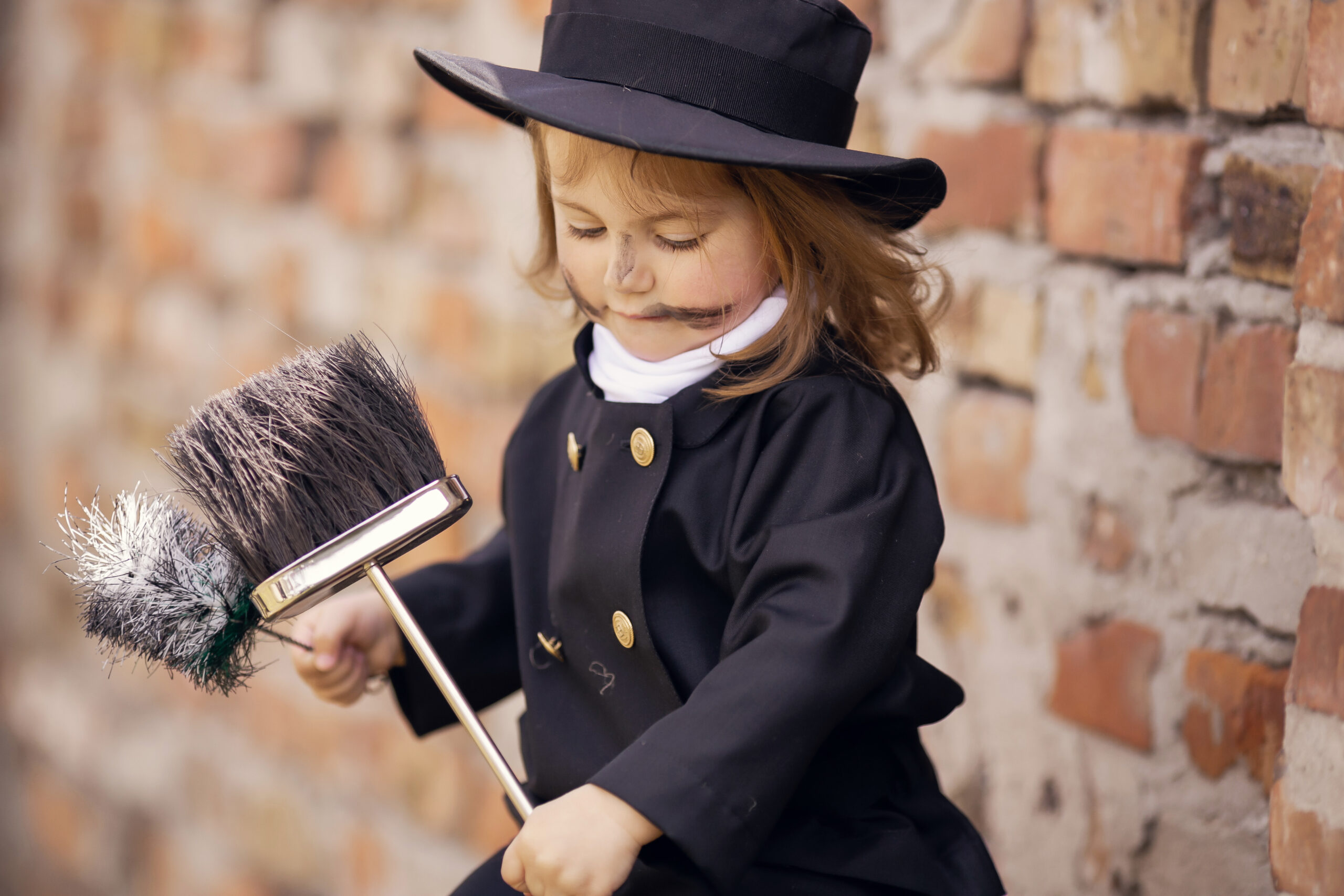 Girl as a chimney sweep against brick wall.